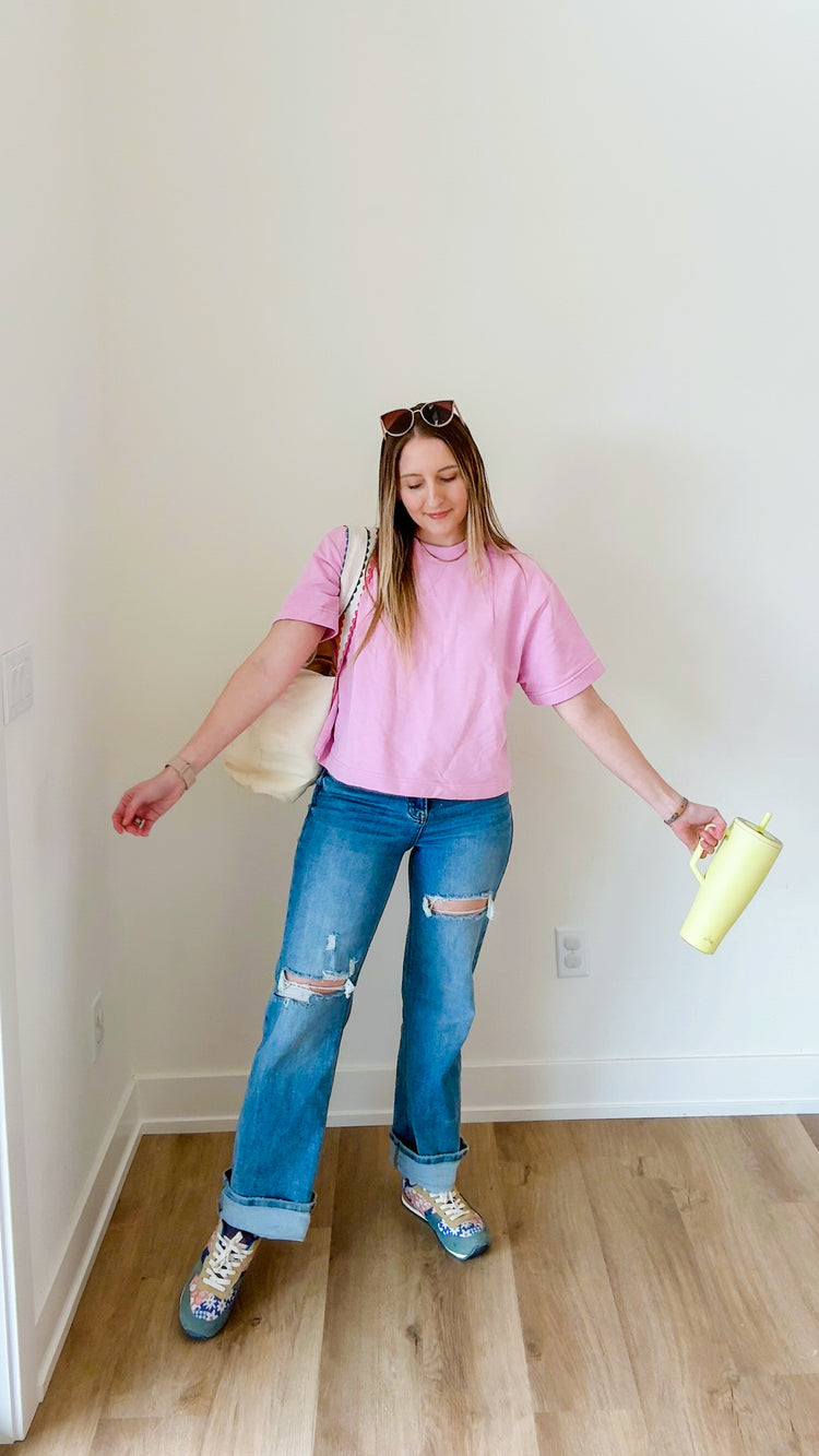 Person wearing a pink shirt and blue jeans holding a yellow object indoors.