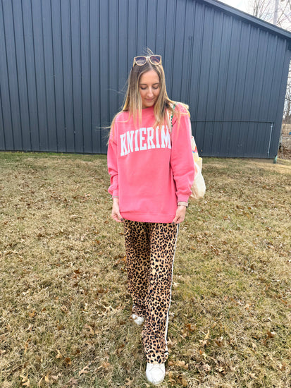 Person wearing a pink sweatshirt and leopard print pants standing in front of a blue building.