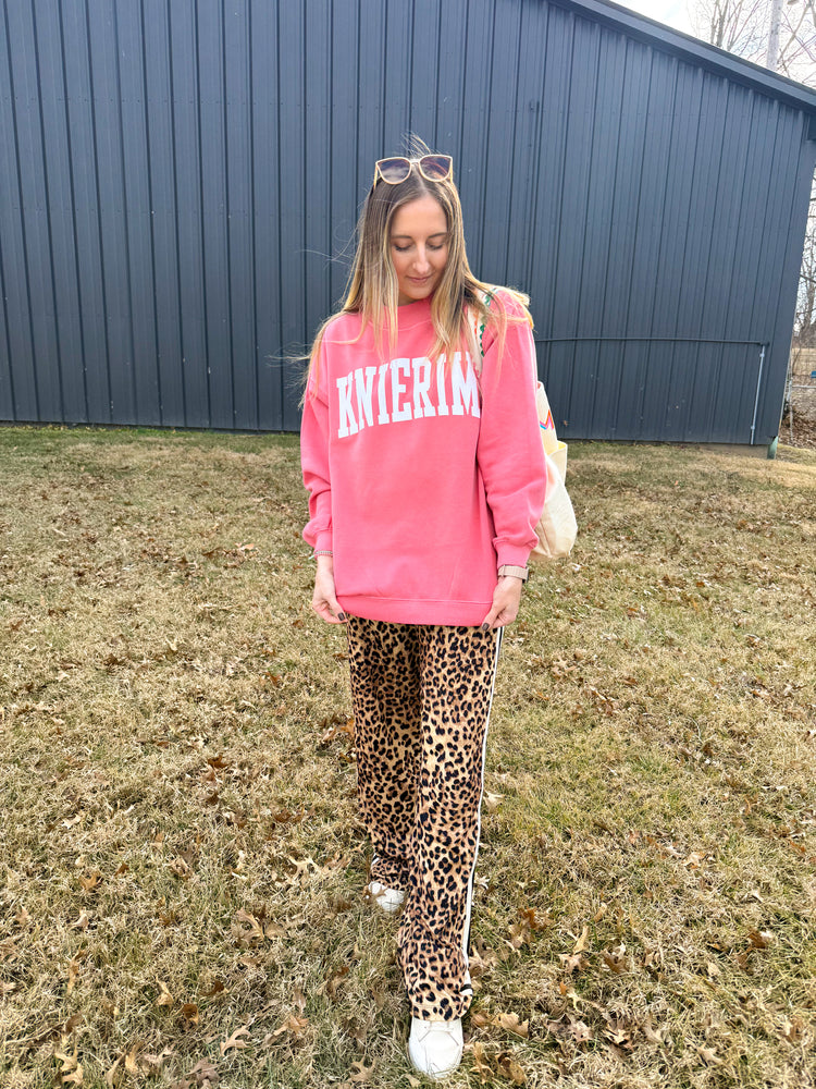 Person wearing a pink sweatshirt and leopard print pants standing in front of a blue building.