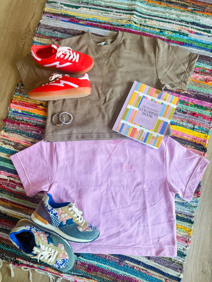 Brown t-shirt, red sneakers, pink shorts, and colorful shoes on a striped rug.