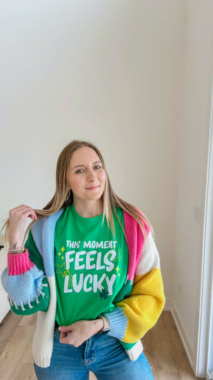 Person wearing a colorful sweater with text, standing indoors.